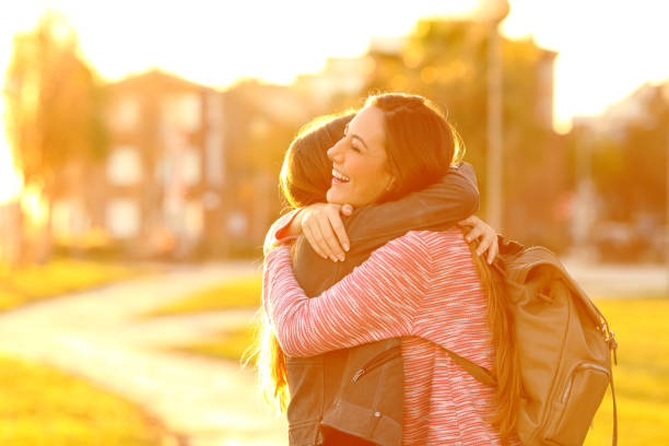 amigos felices del encuentro y abrazando en un parque al atardecer - warm welcome fotografías e imágenes de stock