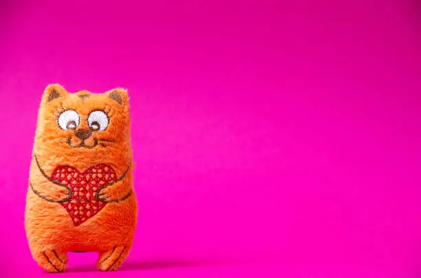 Orange plush cat with red heart in his hands so cute on the pink background. Happy Valentines day