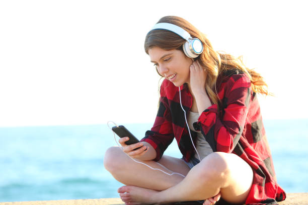 nastoletnia dziewczyna słuchająca muzyki siedzącej na plaży - full song zdjęcia i obrazy z banku zdjęć
