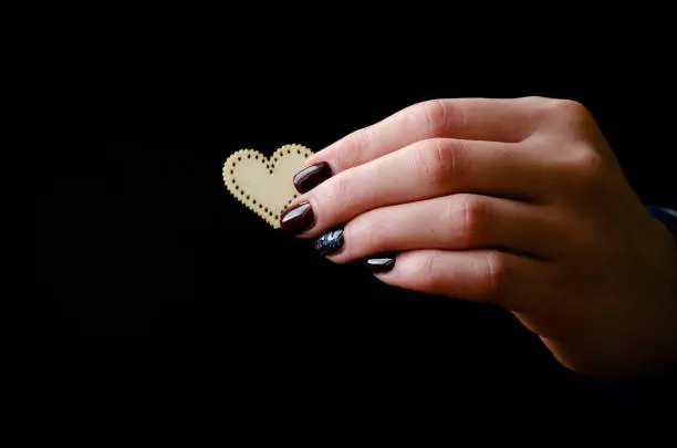 Female hand giving wooden heart on the black background, close up