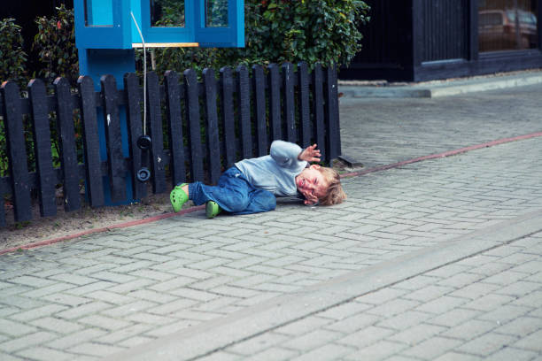 A small cute boy or toddler lays on a pavement next to a public phone booth crying and has major tantrum. stock photo