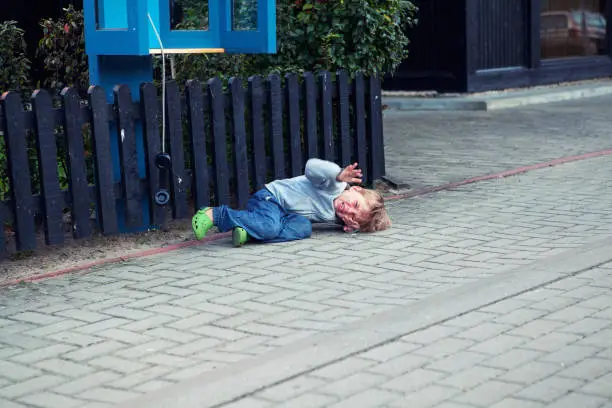 Nida, Lithuania - September 3, 2012: beautiful young boys lays on a sidewalk and cries heartily waving his hands because he was asked to hang a telephone receiver and come to parents.