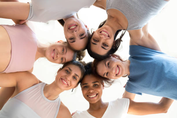 Excited girls hug at training involved in motivational activity Low angle of smiling toned girls stand in circle hugging looking at camera, excited female yogi embrace, feel motivated at yoga session, happy women involved in teambuilding show unity and support low quality of life stock pictures, royalty-free photos & images