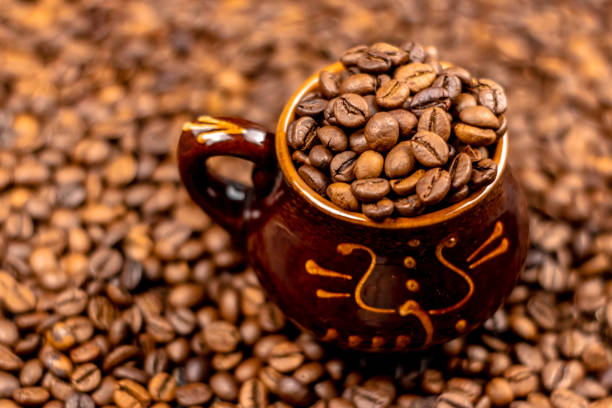 istock Coffee beans in brown ceramic cup on wooden black table. Side view, soft selective focus, copy space. 1127549411