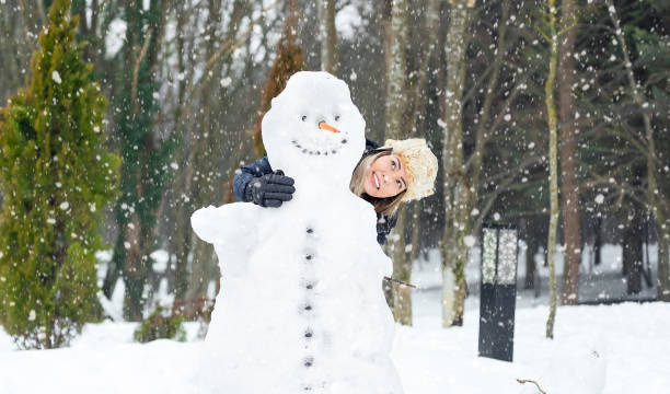Happy woman with long hair  in colorful ski costume resting after hiking trip in the snowcapped mountains and sitting on the bench near the handmade Snowman during sunny frozen winter day