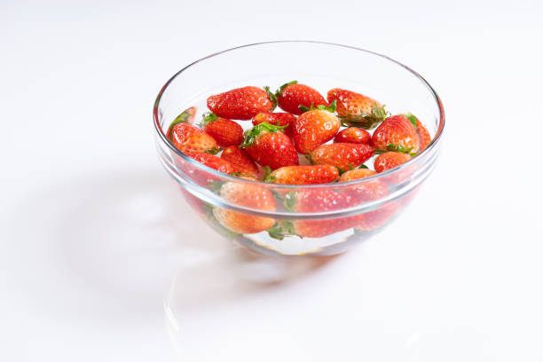 frische erdbeeren in wasserschüssel auf weißem hintergrund - washing fruit preparing food strawberry stock-fotos und bilder