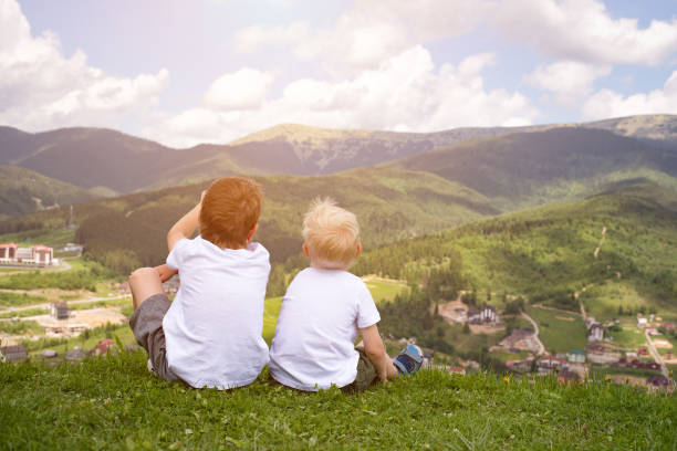 istock Two boys sitting on a hill and looking at the mountains. Back view 1127558984
