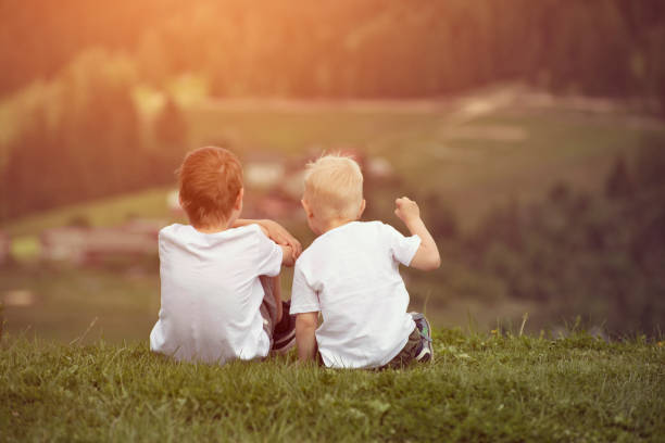 istock Two boys sit on the hill and talking cheerfully. Back view 1127558989