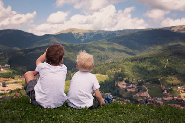 istock Two boys sitting on a hill and looking at the mountains. Back view 1127558991