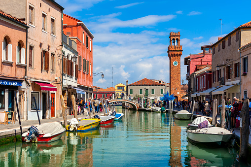 MURANO, ITALY - APRIL 20, 2016: People walking narrow canal with boats among old colorful houses of Murano - famous island in Venetian Lagoon, popular tourist destination.