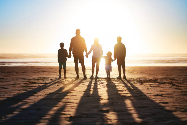 Love keeps a family flourishing Rearview shot of a happy young family bonding on the beach at sunset family holding hands stock pictures, royalty-free photos & images