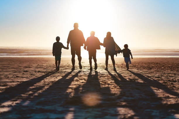 Never miss a sunset Rearview shot of a happy young family going for a walk together along the beach family holding hands stock pictures, royalty-free photos & images