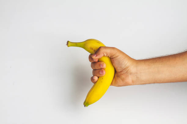 primo piano dell'uomo che tiene la banana contro lo sfondo bianco - men banana holding cut out foto e immagini stock