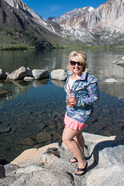 blonde woman holding a tea poses by convict lake in californias sierra nevada mountains in the spring - convict lake imagens e fotografias de stock