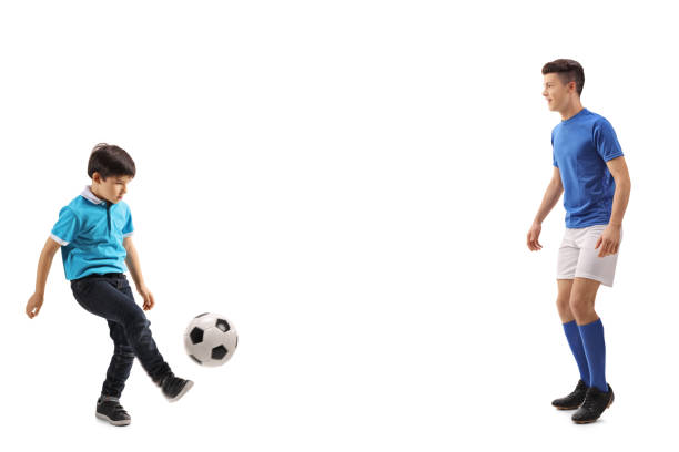 Full length shot of a little boy playing soccer with an older boy isolated on white background