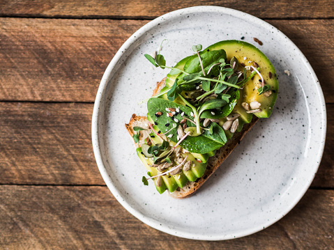 Green healthy sandwich made from spinach, sprouts, avocado and various seeds on a white plate