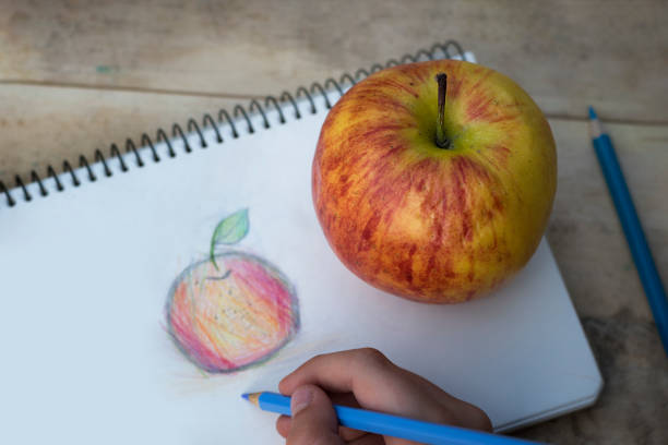 istock Children's hands draw an apple with colored pencils. Top view 1127572217
