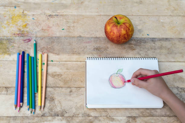 istock Children's hands draw an apple with colored pencils. Top view 1127572219