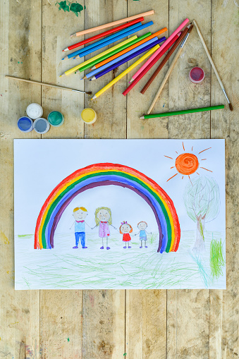 Happy family concept. Sheet with a pattern on a wooden table: parents and children hold hands against background of rainbow and sunny sky