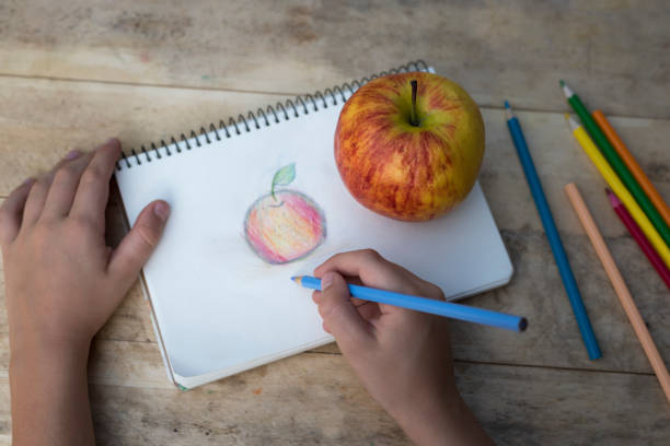 istock Children's hands draw an apple with colored pencils. Top view 1127572229