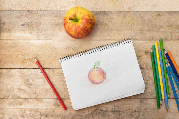 istock Children's drawing, apple and colored pencils. Wooden table. Top view 1127572278