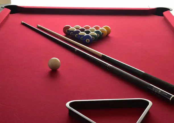 Billiard balls with numbers on them on a red pool table with two cues, a white cue ball and a black rack.