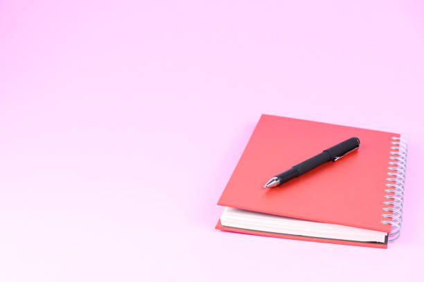 istock Red book or notebook with black pen isolated on pink pastel background 1127575210