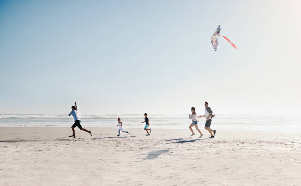 Family at play on a bright sunny day Shot of a happy young family of five flying a kite together on the beach kite toy stock pictures, royalty-free photos & images
