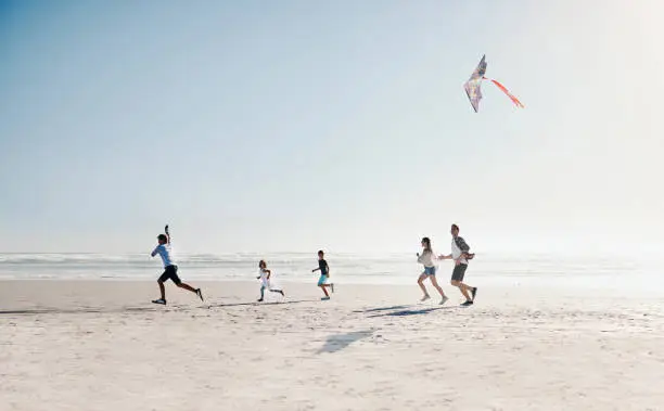Shot of a happy young family of five flying a kite together on the beach