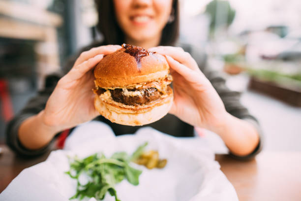 frau essen beef-burger - burger stock-fotos und bilder