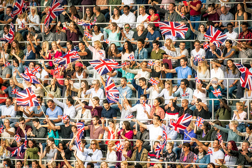 People with Great Britain flags on a stadium cheering for their team during a sports event.