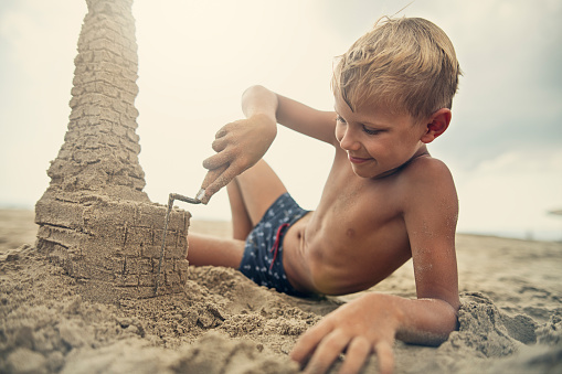 Little boy carving a sandcastle on beach.\nNikon D850