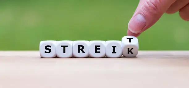 Hand turns a dice and changes the German word "STREIT" ("to argue" in English) to "STREIK" ("on strike" in English). Symbolize that a disagreement can lead to a strike.