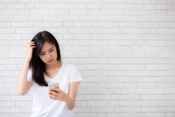 Portrait of asian woman have bored and displeased with something looking smart phone standing on cement brick background, girl with expression and emotion, lady tired or problem. stock photo