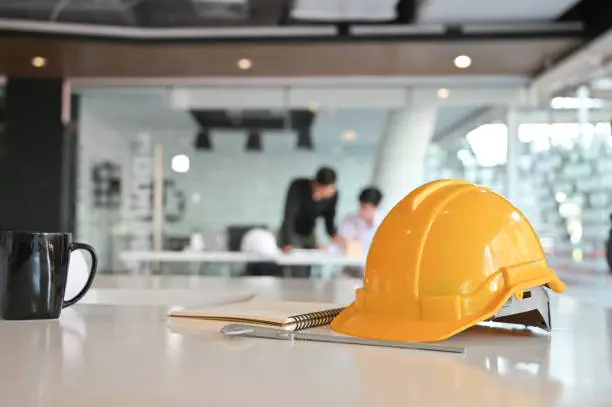 Photo of Architectural Office desk construction project with drawing equipment and engineer helmet.