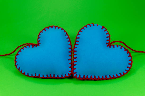 Heart shaped hand stitched textile hearts made of blue fabric and sewed with red threads on green chromakey background for romantic or Valentines concepts