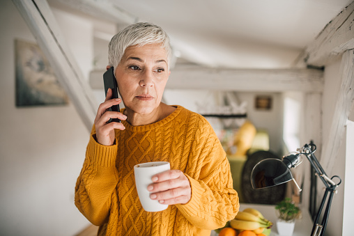 Serious mature woman using mobile phone and drinking coffee