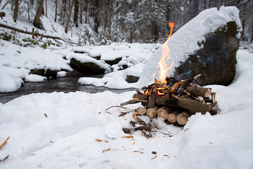 Fire on the snow near the mountain stream, in the winter forest. Winter landscape. Concept adventure.