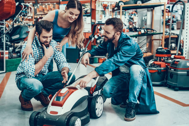 Salesman with Customers in Power Tools Store. Salesman is Bearded Caucasian Man. Customers is Caucasian Couple of Man and Woman. Seller is Showing New Lawn Mower to Clients. Persons is Smiles.