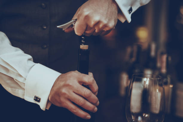 Sommelier is Opened Wine Bottle with Corkscrew Experienced Sommelier is Working in Restaurant. Sommelier is Opened Bottle with Corkscrew. Bottle with Red Wine. Sommelier is Caucasian Man. Man is Wearing Special Uniform. Closeup. uncork wine stock pictures, royalty-free photos & images