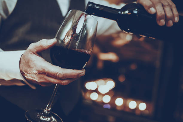 Sommelier is Pouring Wine from Bottle to Glass Experienced Sommelier is Working in Restaurant. Sommelier is Pouring Wine from Bottle to Glass. Red Wine. Sommelier is Caucasian Man. Person is Wearing Special Uniform. Closeup View. maroon stock pictures, royalty-free photos & images