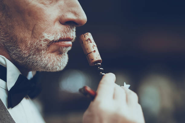 Sommelier is Sniffing Cork with Corkscrew of Wine Experienced Sommelier is Working in Restaurant. Sommelier is Sniffing Cork with Corkscrew of Wine. Sommelier is Mature Caucasian Man. Person is Wearing Special Uniform. Closeup View. uncork wine stock pictures, royalty-free photos & images