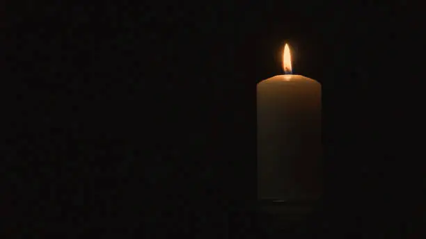 Burning candle. The light from the fire. Black background. Isolated. Mystery and mystique. Feelings and emotions.