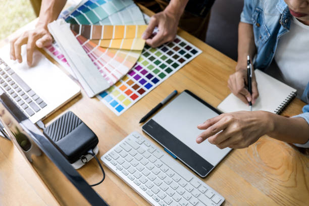 istock Team of young colleagues creative graphic designer working on color selection and drawing on graphics tablet at workplace, Color swatch samples chart for selection coloring 1127612454