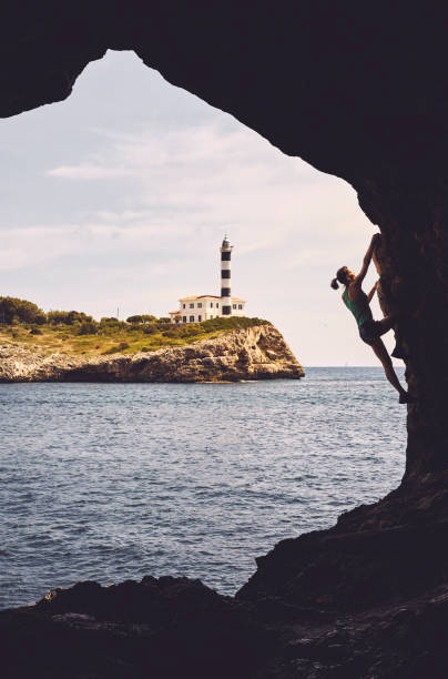 Silhouette of a woman climbing in a cave, Portocolom Lighthouse in background, color toning applied, Mallorca, Spain.