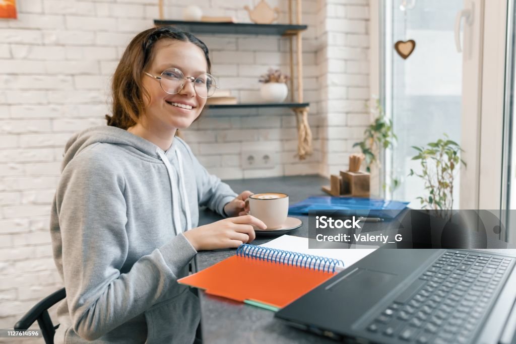 Retrato de joven estudiante, estudiante de secundaria en cafetería con ordenador portátil y taza de café, chica es estudiando, escribiendo en el cuaderno - Foto de stock de 14-15 años libre de derechos