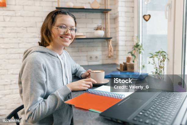 Retrato De Joven Estudiante Estudiante De Secundaria En Cafetería Con Ordenador Portátil Y Taza De Café Chica Es Estudiando Escribiendo En El Cuaderno Foto de stock y más banco de imágenes de 14-15 años