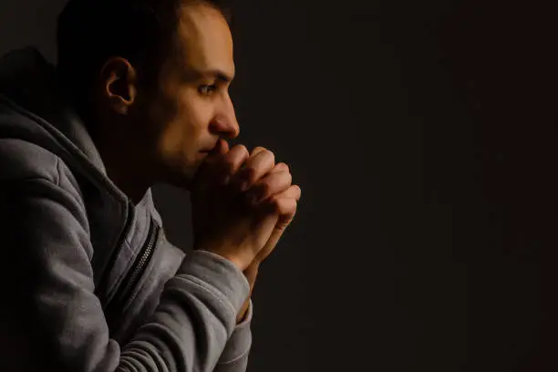 Photo of Religious young man praying to God on dark background, black and white effect