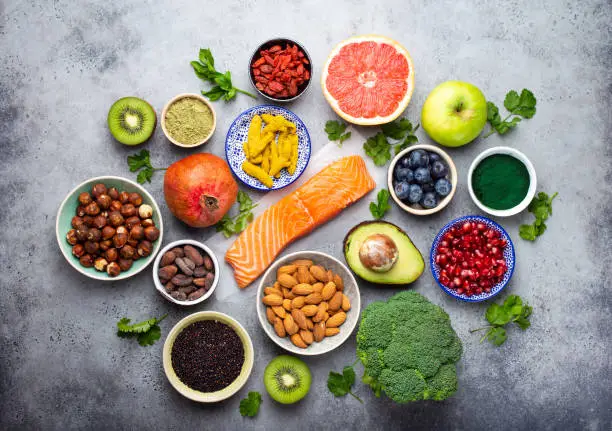 Selection of healthy products and superfoods: salmon, fruit, vegetables, berries, goji, spirulina, matcha, quinoa, chia seeds, nuts. Clean eating concept, gray background, top view, close up
