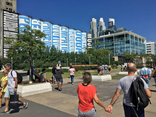 Buenos Aires, Argentina - February 3, 2019: People walking in the street and enjoying the evening in the fancy Puerto Madero neighborhood. Its wide new streets and promenades next to the river make them a perfect place for a city break. At the far left side an installation made by Barbara Kruger for the Art Basel Cities Buenos Aires can be seen